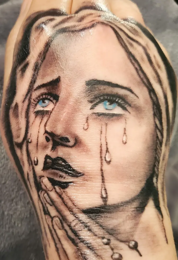 Realistic portrait of praying hands and a woman's face tattooed on an arm