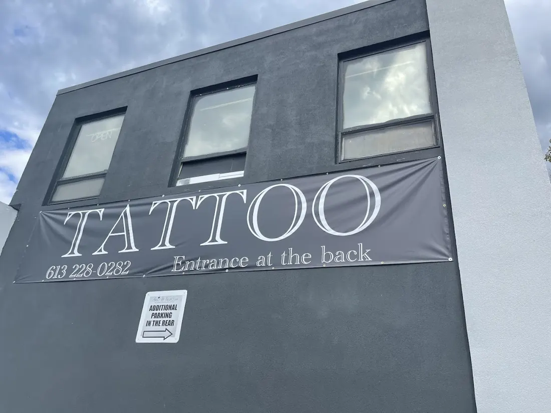 Grey building wall with a TATTOO banner showing the phone number and the words entrance at the back